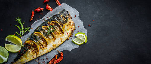 Grilled mackerel fish with lime on a black background, copy space fried fish and vegetables