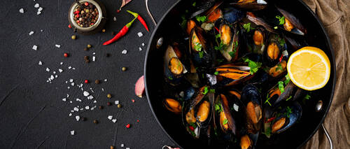 Mussels cooked in wine sauce with herbs in a frying pan on a black background. Flat lay. Top view.