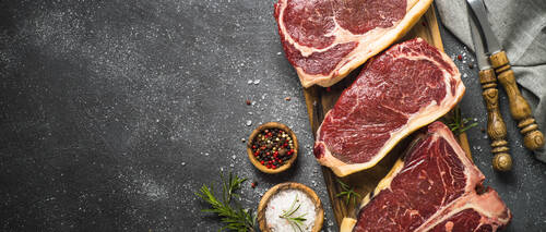 Raw meat beef steak. Black angus prime meat set - ribeye, striploin, t-bone steaks on cutting board. Top view on black table with copy space.
